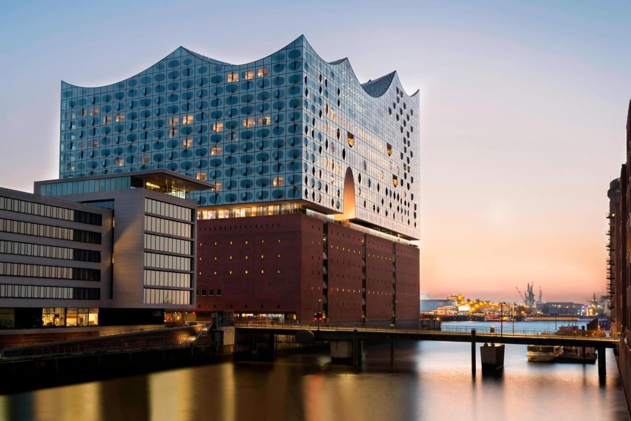 The Westin Hamburg Elbphilharmonie Hotel Ngoại thất bức ảnh The photo shows a modern architectural structure located by a body of water, possibly a river or canal. The building features a unique wavy roofline and a facade made of glass and other materials, giving it a contemporary look. It is likely a cultura