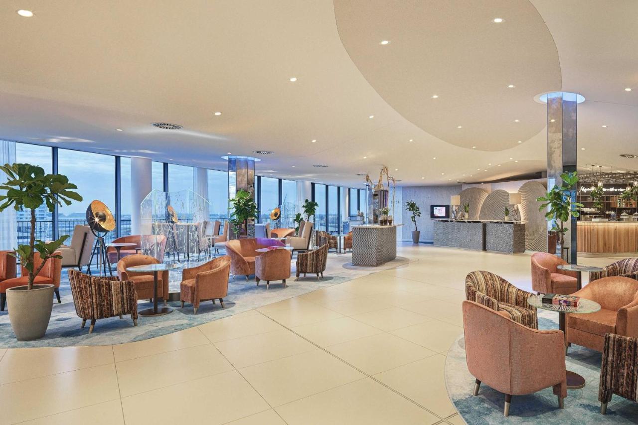 The Westin Hamburg Elbphilharmonie Hotel Ngoại thất bức ảnh The image shows a modern, stylish interior, likely from a hotel or upscale lounge. The space features large windows that allow natural light to flood in, offering a view of the outside. There's a mix of comfortable seating arrangements, including sev