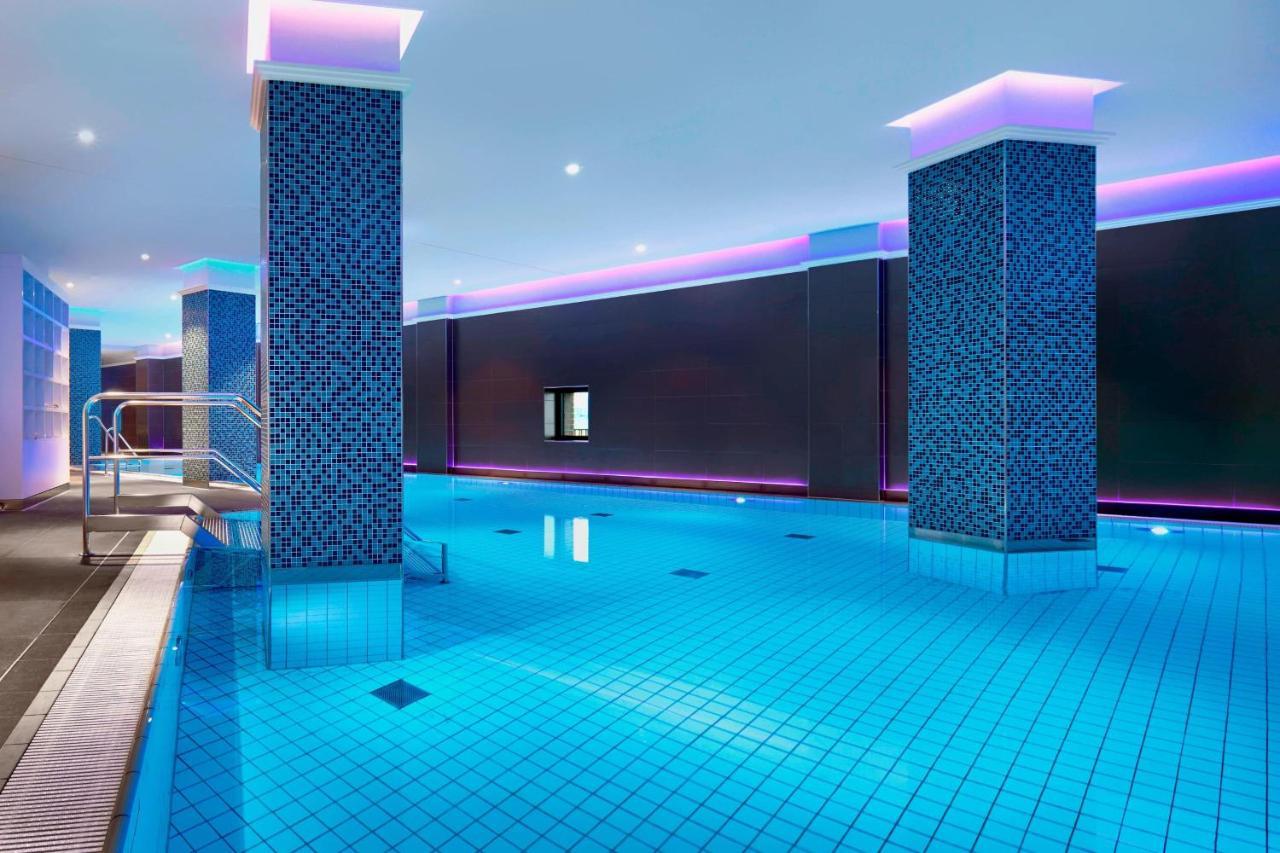 The Westin Hamburg Elbphilharmonie Hotel Ngoại thất bức ảnh The image shows a swimming pool area that features a modern, upscale design. The pool has bright blue tiles reflecting the water, creating a vibrant atmosphere. There are two columns dressed in a similar blue tile pattern, and the walls are adorned w