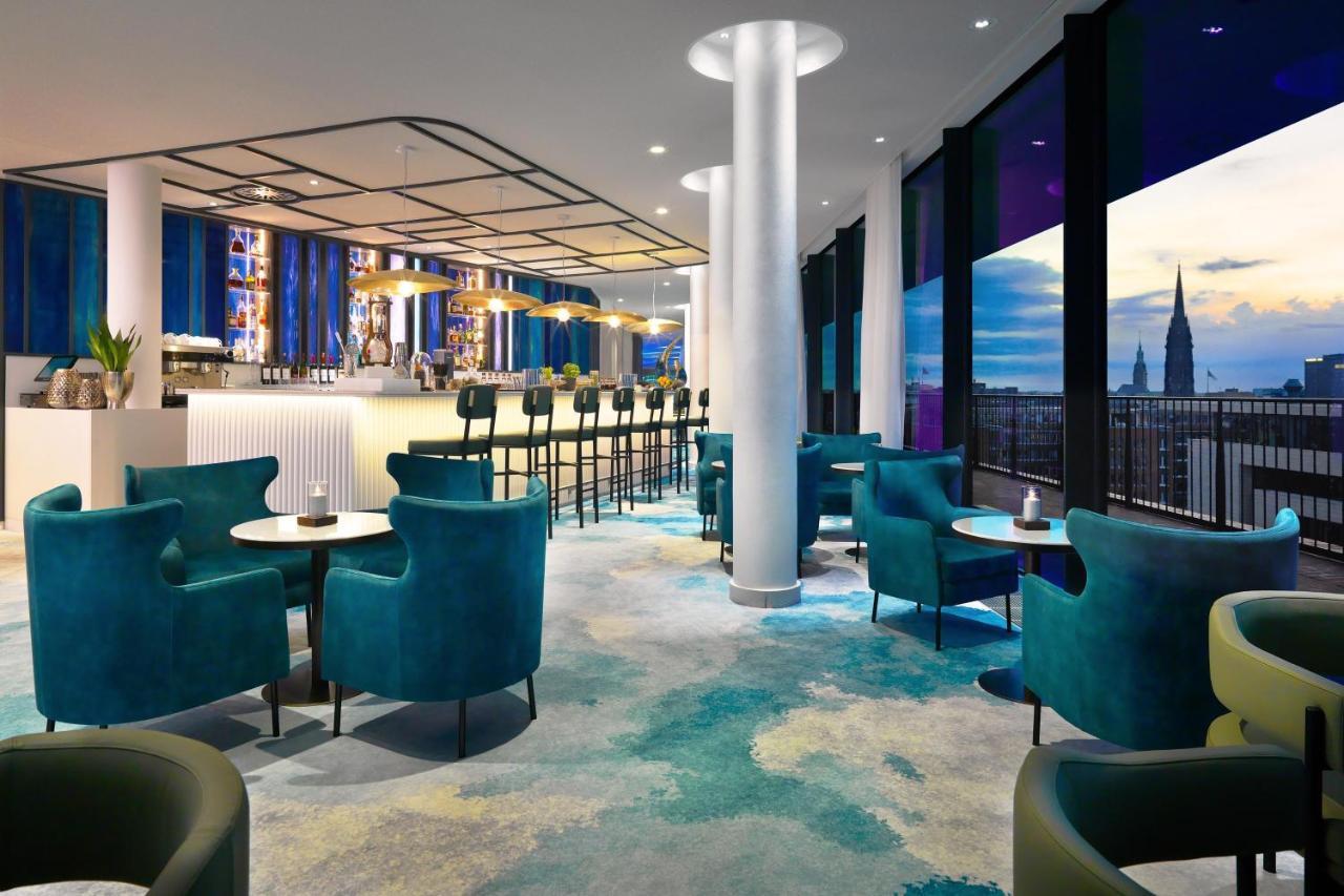 The Westin Hamburg Elbphilharmonie Hotel Ngoại thất bức ảnh The photo shows a modern lounge or bar area with a stylish design. It features plush turquoise chairs and small tables arranged around the space. In the background, there's a long bar with seating, illuminated by soft lighting. Large windows provide 
