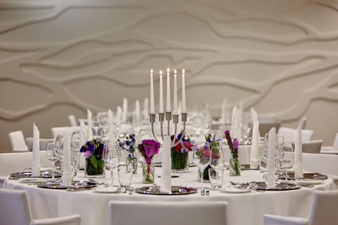 The Westin Hamburg Elbphilharmonie Hotel Ngoại thất bức ảnh The photo depicts an elegantly set round dining table. In the center, there is a candelabra with several tall candles, providing a soft, warm light. Surrounding the candelabra are small glass vases filled with colorful flowers, adding a vibrant touch