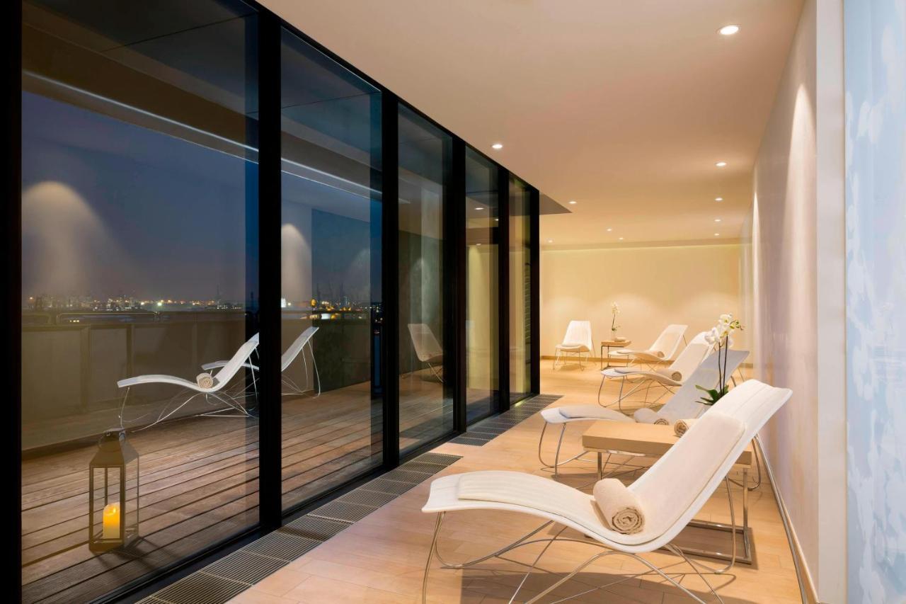 The Westin Hamburg Elbphilharmonie Hotel Ngoại thất bức ảnh The photo shows a modern, stylish indoor space with large glass windows that offer a view of the night. The area is illuminated softly, highlighting a sleek and minimalist design. There are several white lounge chairs arranged on a wooden deck, creat