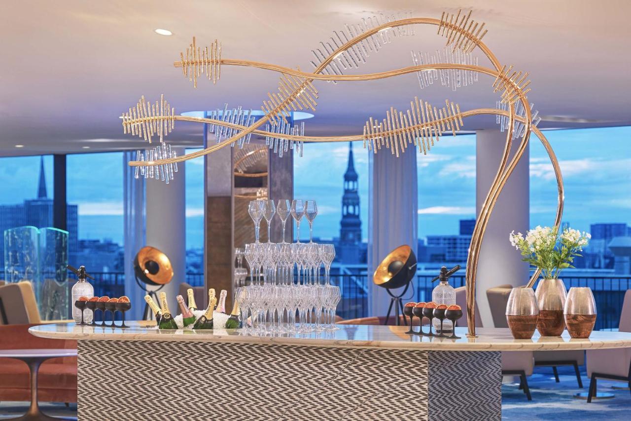 The Westin Hamburg Elbphilharmonie Hotel Ngoại thất bức ảnh The photo depicts a stylish bar setup in a modern venue. The bar features an elegant design with a patterned front and a sleek countertop. Above the bar, there is a striking decorative element that resembles a stylized tree or wave, made from metalli