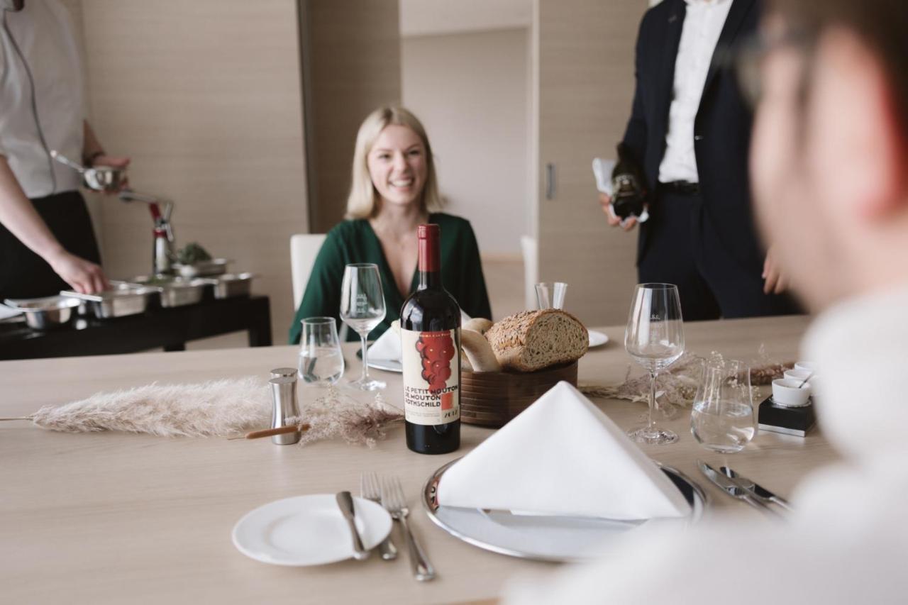 The Westin Hamburg Elbphilharmonie Hotel Ngoại thất bức ảnh The image shows a dining setting with a woman smiling at the table. She is seated in front of a bottle of red wine that has a distinctive label. There is also bread and a neatly arranged table setting, including plates and glasses. In the background,