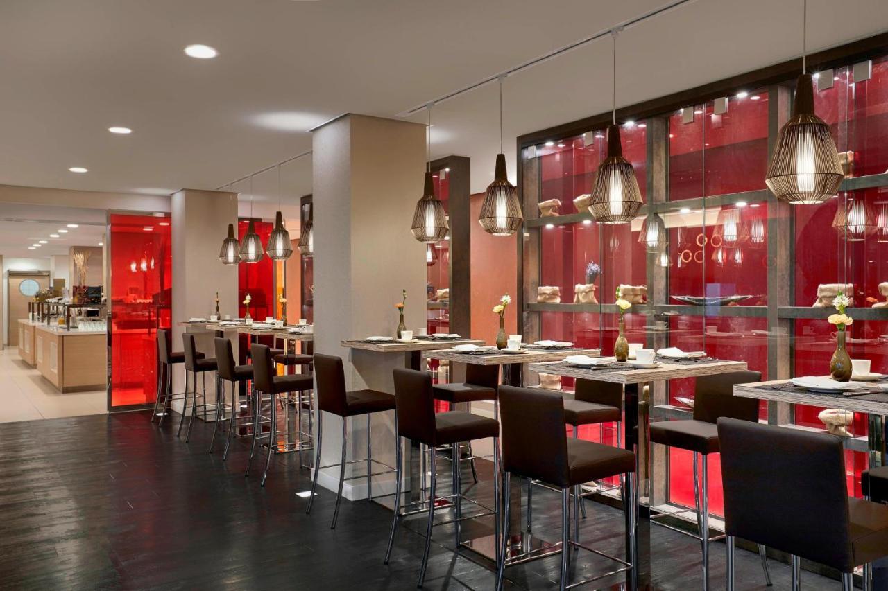 The Westin Hamburg Elbphilharmonie Hotel Ngoại thất bức ảnh The photo shows a modern restaurant interior featuring a sleek, contemporary design. There are high tables with bar stools arranged along one side, illuminated by stylish hanging pendant lights. The color scheme includes warm tones, with red accents 