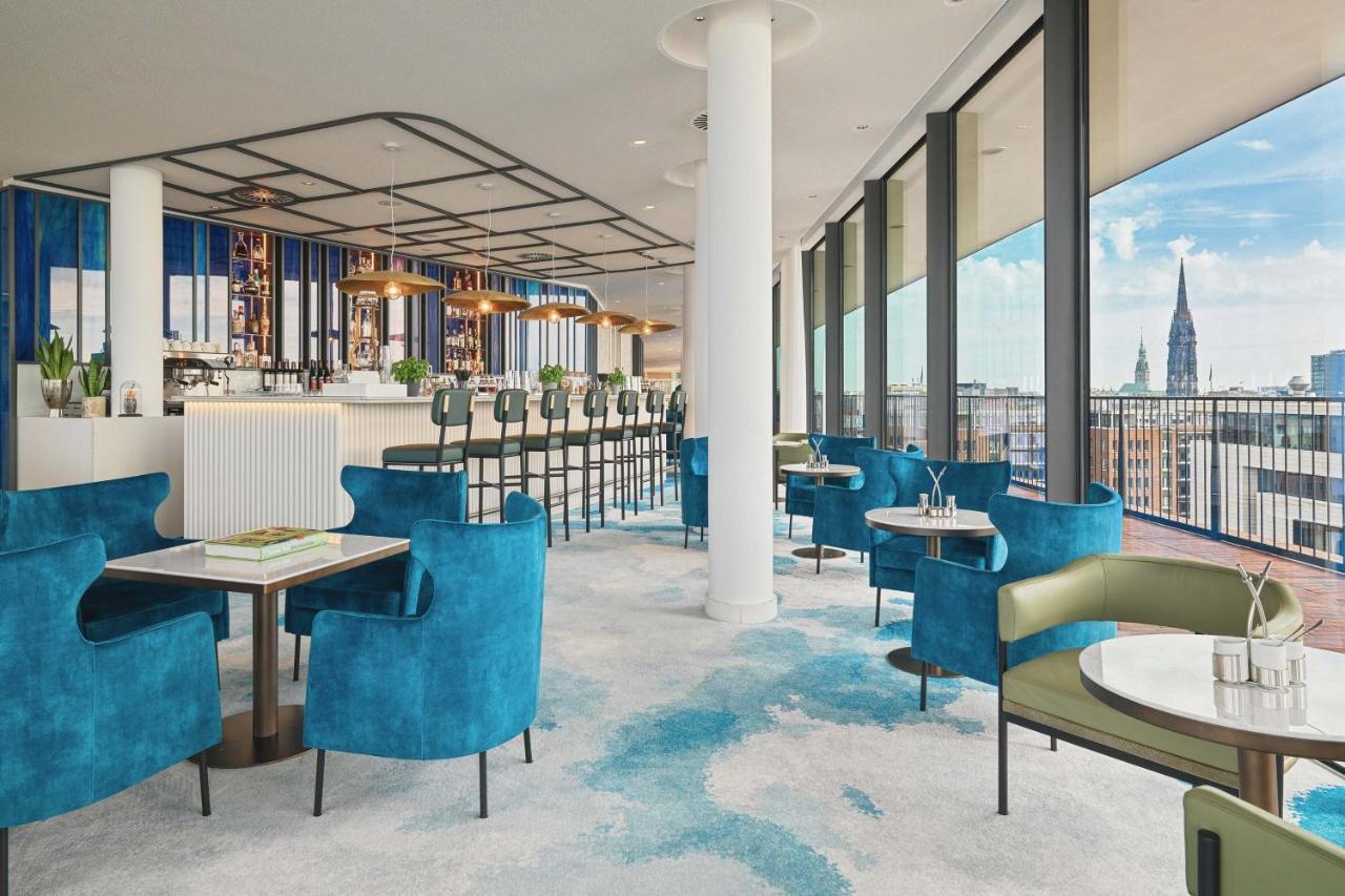 The Westin Hamburg Elbphilharmonie Hotel Ngoại thất bức ảnh The image shows a stylish and modern restaurant interior. There are several tables with blue and green chairs, creating a cozy atmosphere. The flooring features a light carpet with abstract patterns. Large windows provide plenty of natural light and 