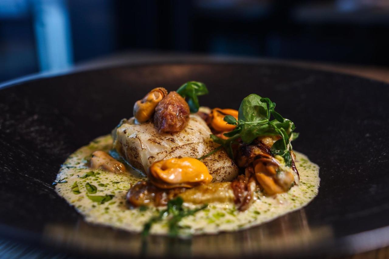 The Westin Hamburg Elbphilharmonie Hotel Ngoại thất bức ảnh The photo shows a beautifully presented plate of food. It features a piece of fish, likely white fish, which is cooked and garnished with various elements. Surrounding the fish are mussels, possibly in their shells, and some sort of sauce, likely a c