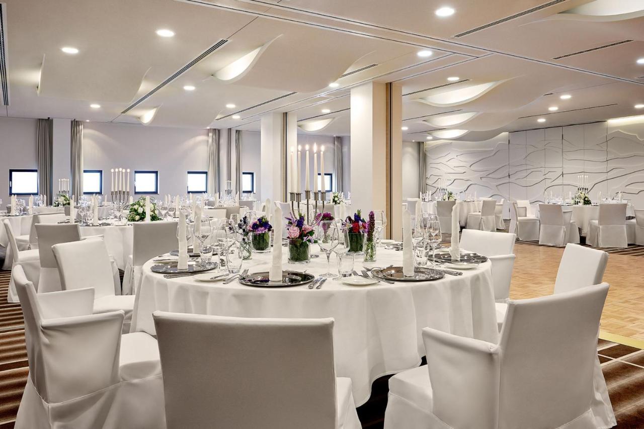 The Westin Hamburg Elbphilharmonie Hotel Ngoại thất bức ảnh The photo depicts a modern banquet or event hall setup. It features round tables covered with white tablecloths, each set with elegant dishware and glassware. The tables are adorned with floral centerpieces, adding a touch of color, and there are tal