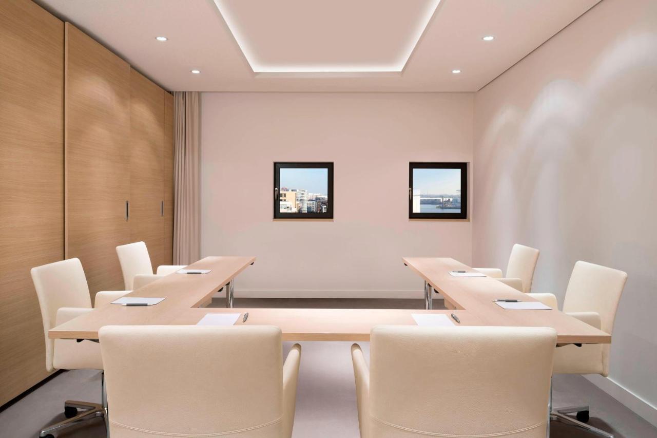 The Westin Hamburg Elbphilharmonie Hotel Ngoại thất bức ảnh The photo shows a modern conference room. It features a long, rectangular table made of light-colored wood, surrounded by several cream-colored chairs. The walls are painted in a light shade, and there are two framed windows on one wall that provide 