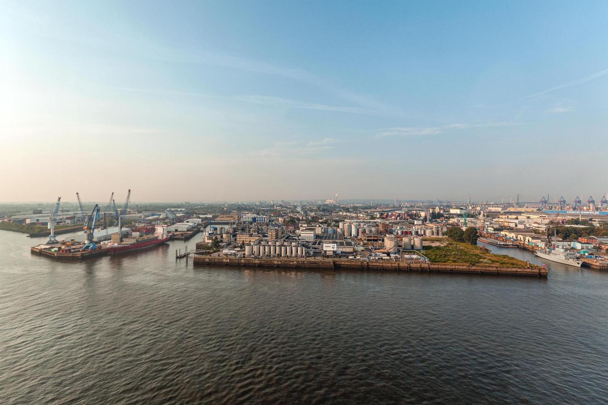 The Westin Hamburg Elbphilharmonie Hotel Ngoại thất bức ảnh The photo shows a coastal area with a large body of water in the foreground. To the left, there are industrial structures like cranes and cargo ships, indicating an active port or shipping area. In the background, there are various buildings, which a
